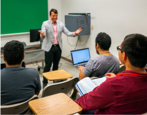 A teach talking to three students in a classroom.