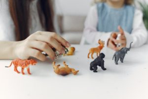 A kindergarten teacher and a young girl play with dinosaur toys