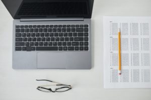 An open laptop beside a test paper with a pencil on top of it.