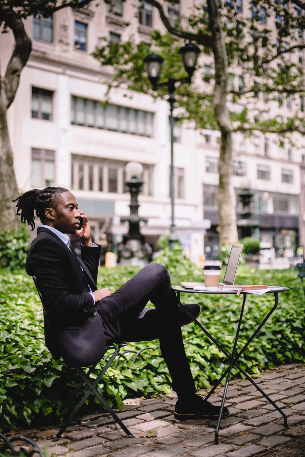 A confident man in a suit talking on the phone in the middle of a park.