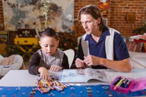 A teacher watching a young child pick out crayons.