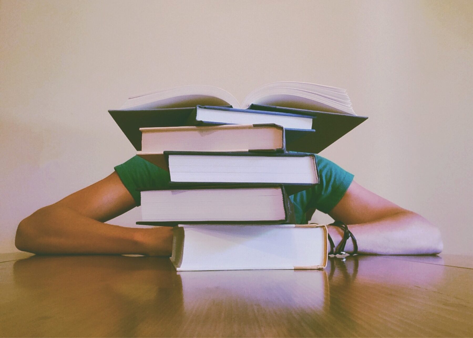 Someone studying behind a pile of books on a desk.