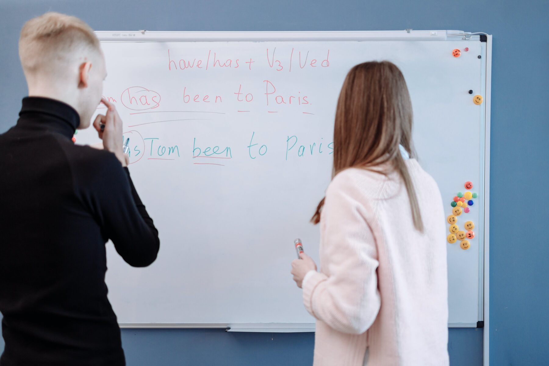 An adult learning English with his teacher writing on the whiteboard. 